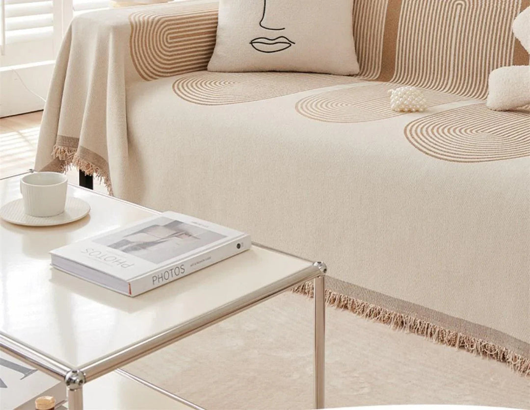 Sandy tan chenille throw blanket draped over a sofa with a book and cup on a coffee table.