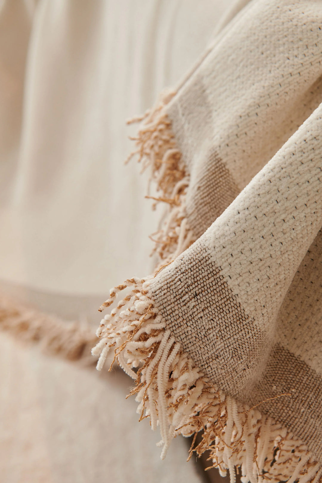 Sandy tan chenille throw blanket with soft tassels draped over a surface.