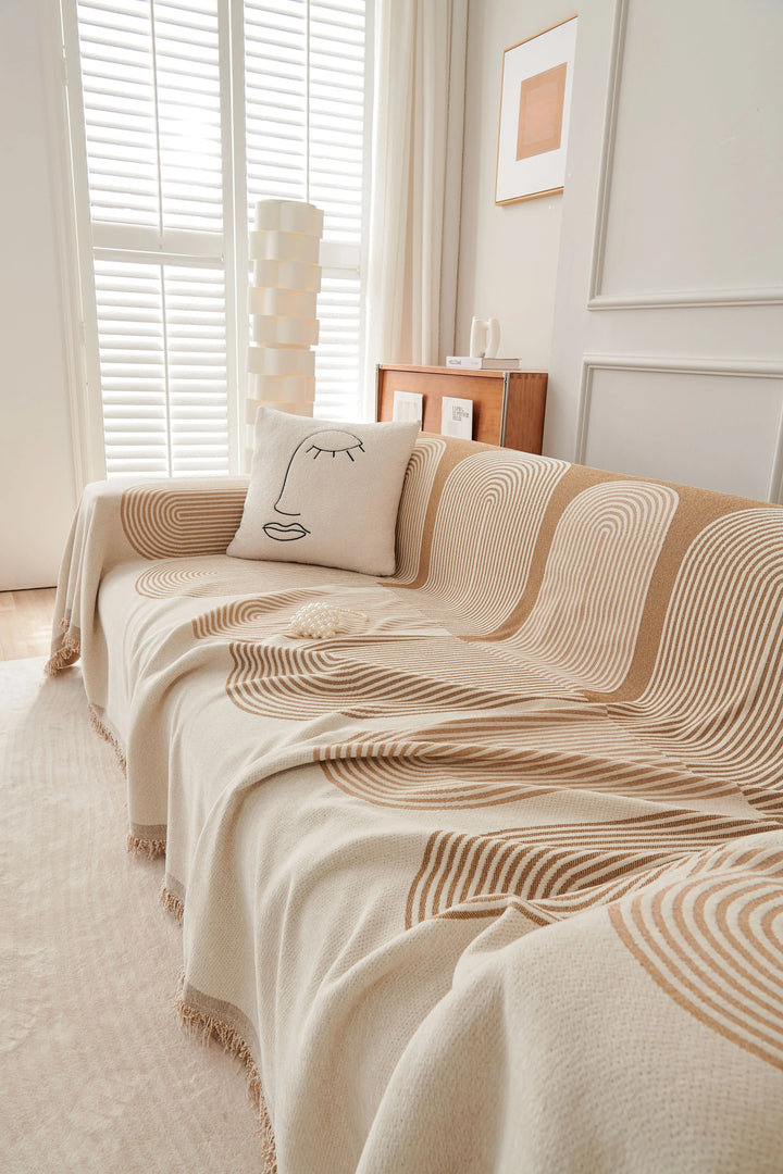 Sandy tan chenille throw blanket with abstract arc pattern draped over a sofa.