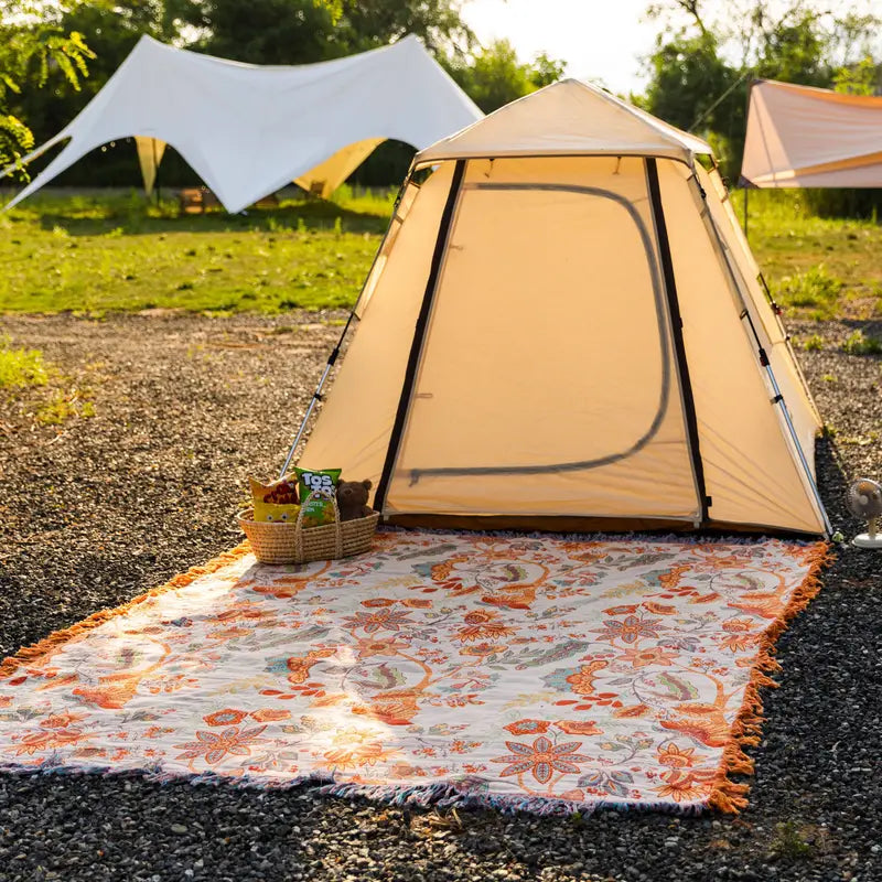 Rustic floral boho cotton blanket spread on the ground in front of a tent.